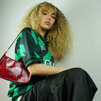 Person wearing a green and black sports jersey with a red handbag, sitting against a plain background.